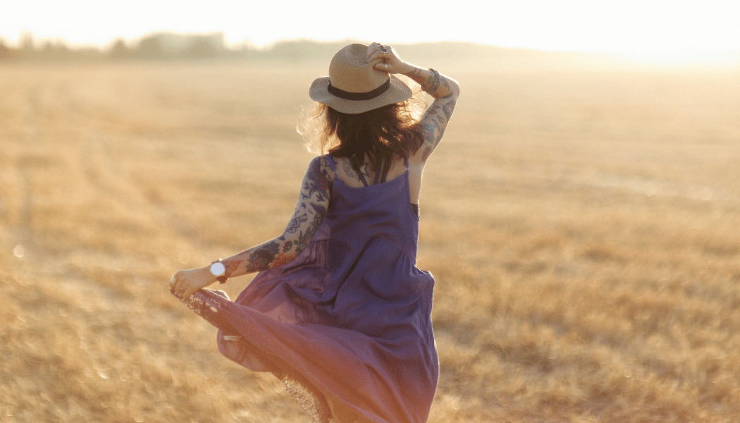 A woman standing in an open field, facing a bright sky
