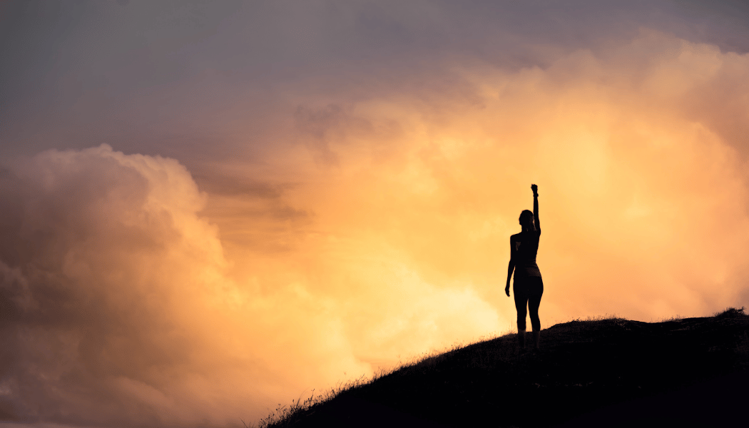 A person standing confidently on a hilltop at sunrise