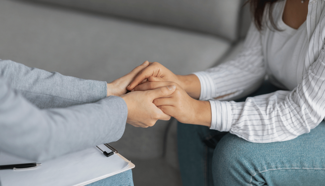 A counselor supportively holding the hands of their client