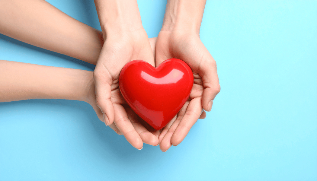 Two pairs of hands support a heart