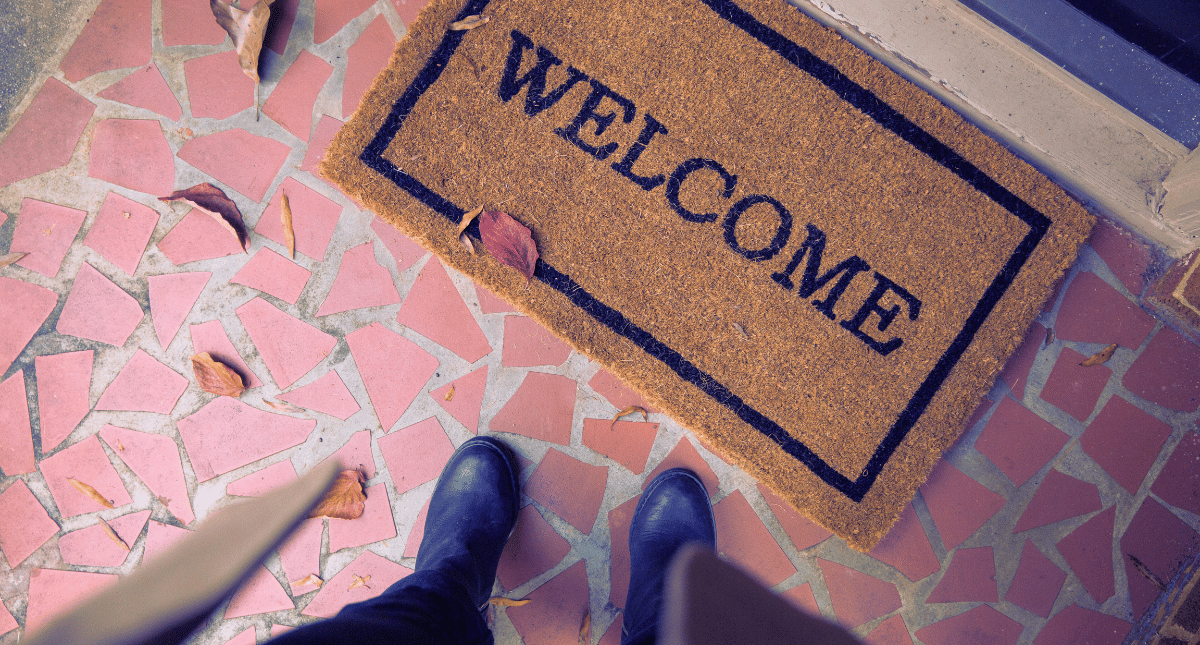 Person standing in front of a door looking down at a mat with 'Welcome' written on it
