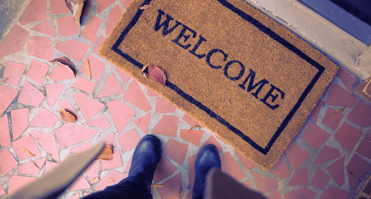 person standing in front of a door looking down at a mat that has 'welcome' written on it